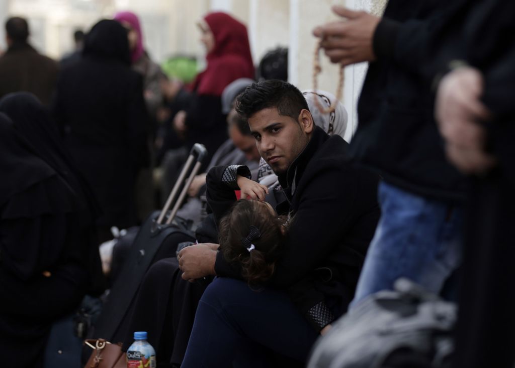 A Palestinian man holds a girl between his arms as he sits in a makeshift station in Khan Younis in the southern Gaza strip on November 18, 2017 as they await clearance to take a bus to travel through the Rafah border crossing with Egypt, after it opened 