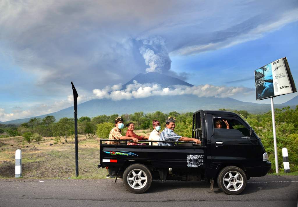 Balinese people ride on an open car past Mount Agung erupting seen from Kubu sub-district in Karangasem Regency, on Indonesia's resort island of Bali on November 27, 2017.  AFP / SONNY TUMBELAKA
