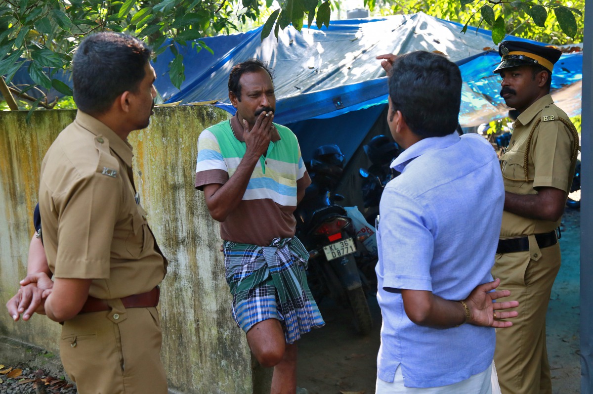 K M Ashokan (2-L), father of 24-year-old Akhila, who converted to Islam in 2016 and took a new name, Hadiya, smokes while speaking with a friend, as police officers stand guard outside his house at Vaikom in the Kottayam district of the southern state of 