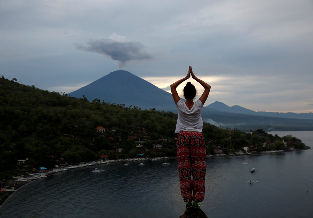 A tourist from Russia poses while a friend takes her photograph with Mount Agung volcano erupting in the background from Amed, Karangasem Regency, Bali, Indonesia, November 30, 2017. REUTERS/Darren Whiteside
