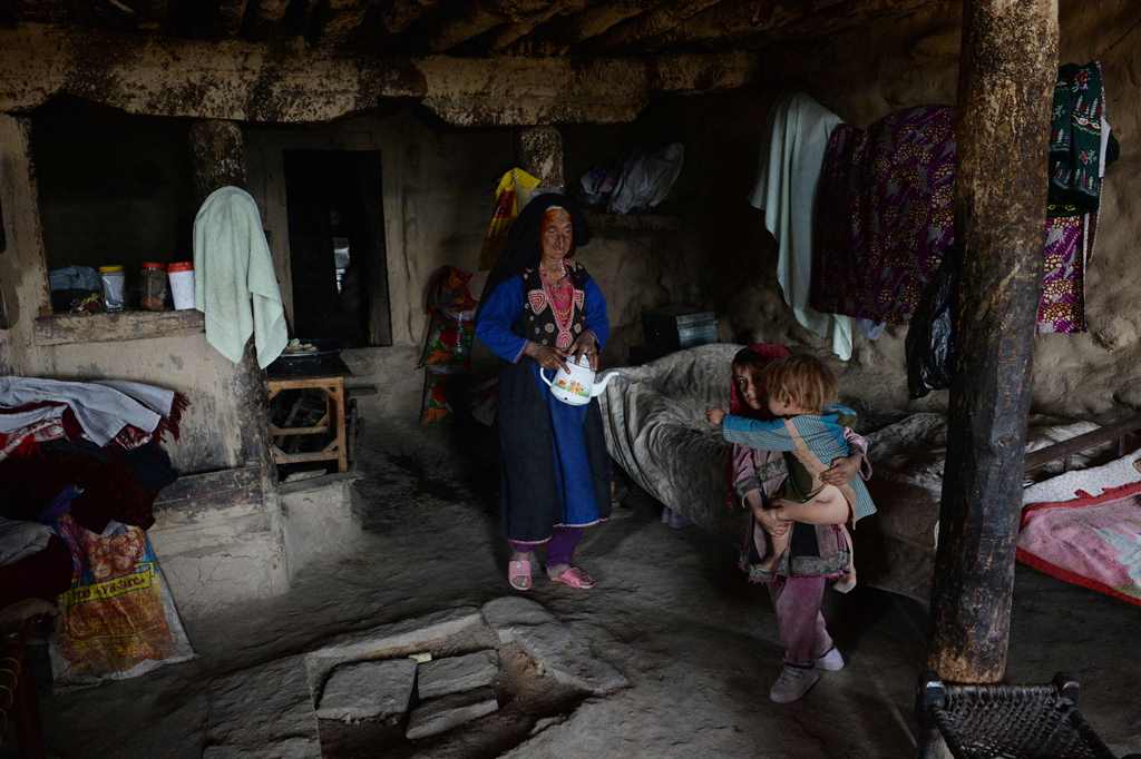 In this photograph taken on October 21, 2017 Afghan widow Janat Bibi, 65, holds a teapot walks inside her mud house in the remote village of Shemol in the eastern province of Nangarhar. AFP / NOORULLAH SHIRZADA 
