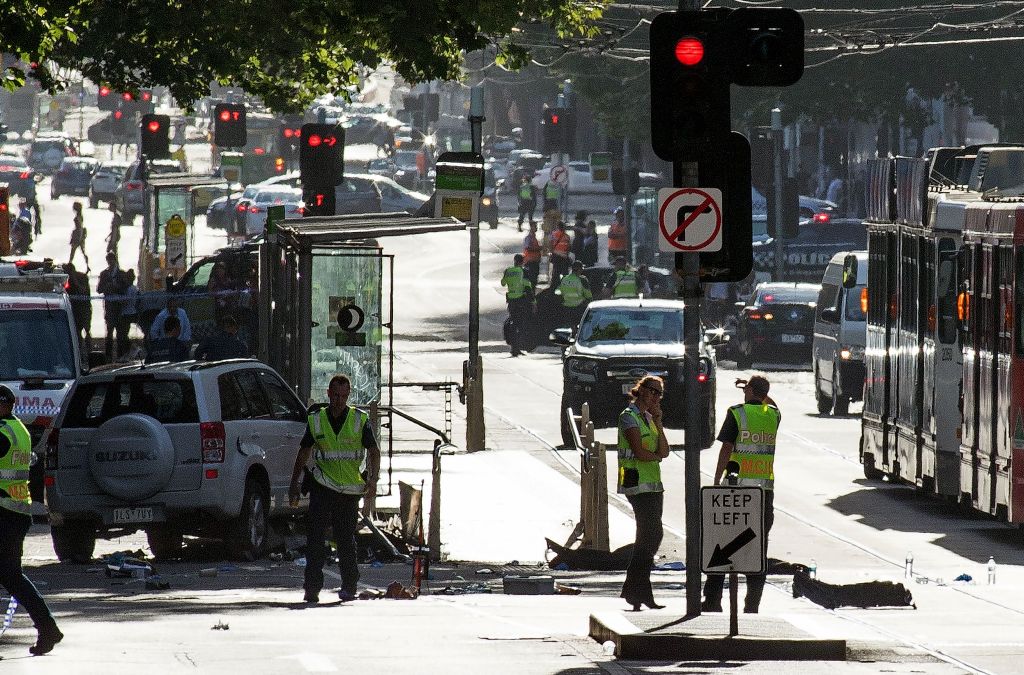 A white SUV (L) sits in the middle of the road as police and emergency personnel work at the scene of where a car ran over pedestrians in Flinders Street in Melbourne on December 21, 2017. / AFP.