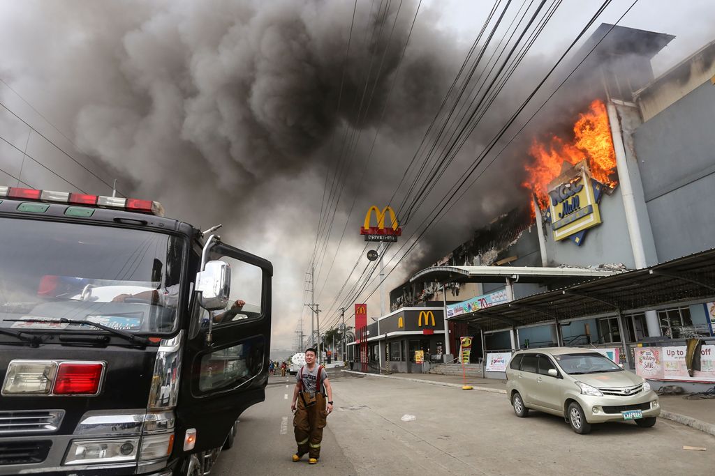 This photo taken on December 23, 2017 shows a firefighter standing in front of a burning shopping mall in Davao City on the southern Philippine island of Mindanao. / AFP.