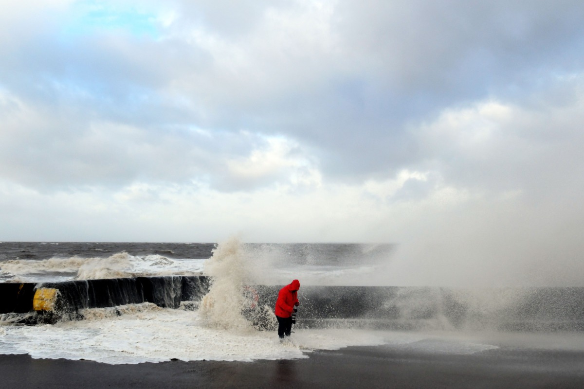 A photographer checks his equipment as waves crash over the tidal wall along the seafront in New Brighton, north west England, on January 3, 2018, as Storm Eleanor swept over the country. Storm Eleanor swept across the country overnight, bringing winds of