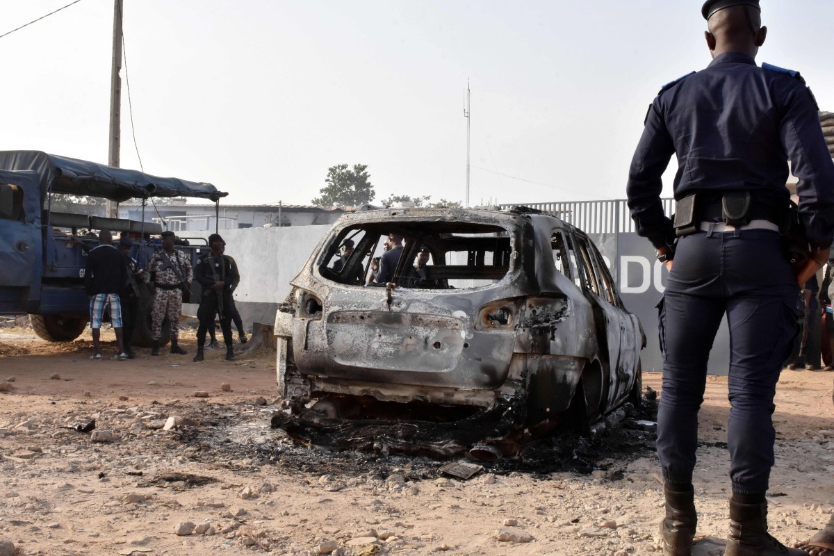 A gendarme stands in front of the wreckage of a burnt car, on January 10, 2018 in front of the CCDO elite military unit centre, a day after gunshots and heavy weapons fire erupted between rival factions within Ivory Coast army.  AFP
