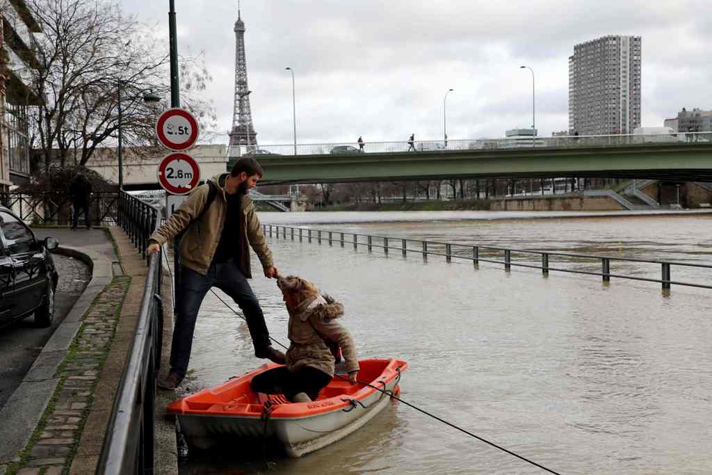 People use a dinghy to access a houseboat after the River Seine burst its banks in Paris on January 24, 2018. / AFP / Ludovic MARIN