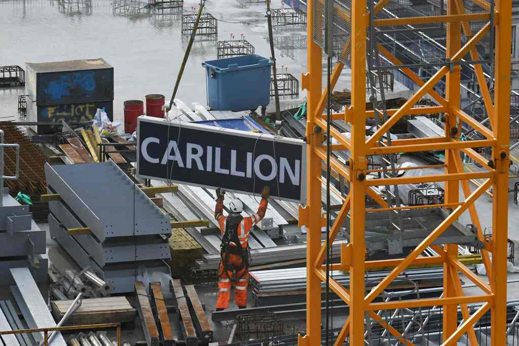 A worker guides down a sign showing the name of liquidated British construction and outsourcing group carillion after it was taken down off a construction crane on a building site in the City of London on January 23, 2017. / AFP / Daniel SORABJI