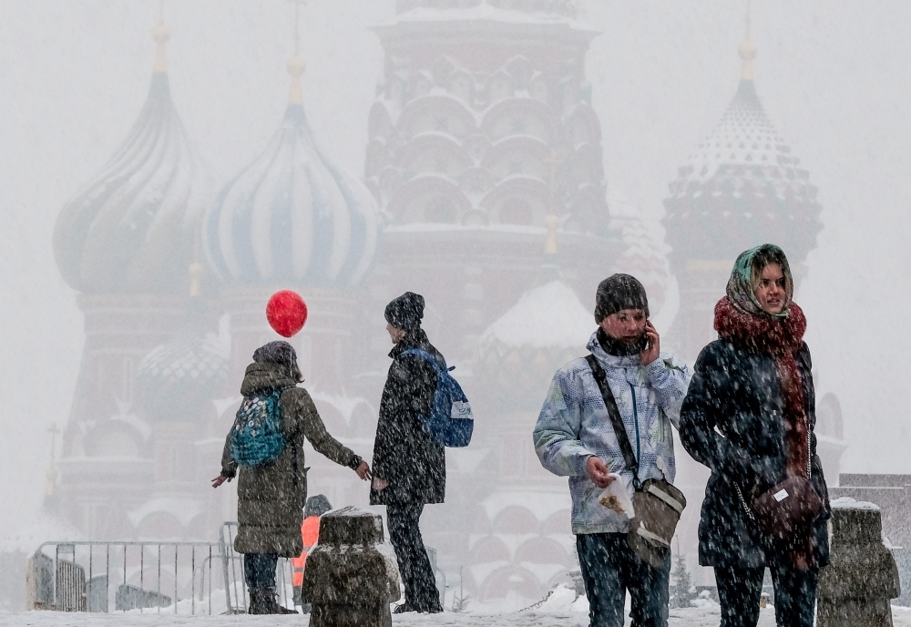 People walk along Red square with St. Basil cathedral seen in the background during snowfall in central Moscow on February 3, 2018. / AFP / Yuri KADOBNOV