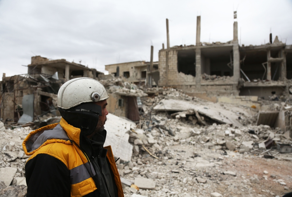 Forty-five-year-old Samir Salim (L), who along with his three brothers are members of the White Helmets rescue forces, looks out at destroyed buildings in the town of Medeira in Syria's rebel-held Eastern Ghouta area on February 12, 2018.   AFP / ABDULMON