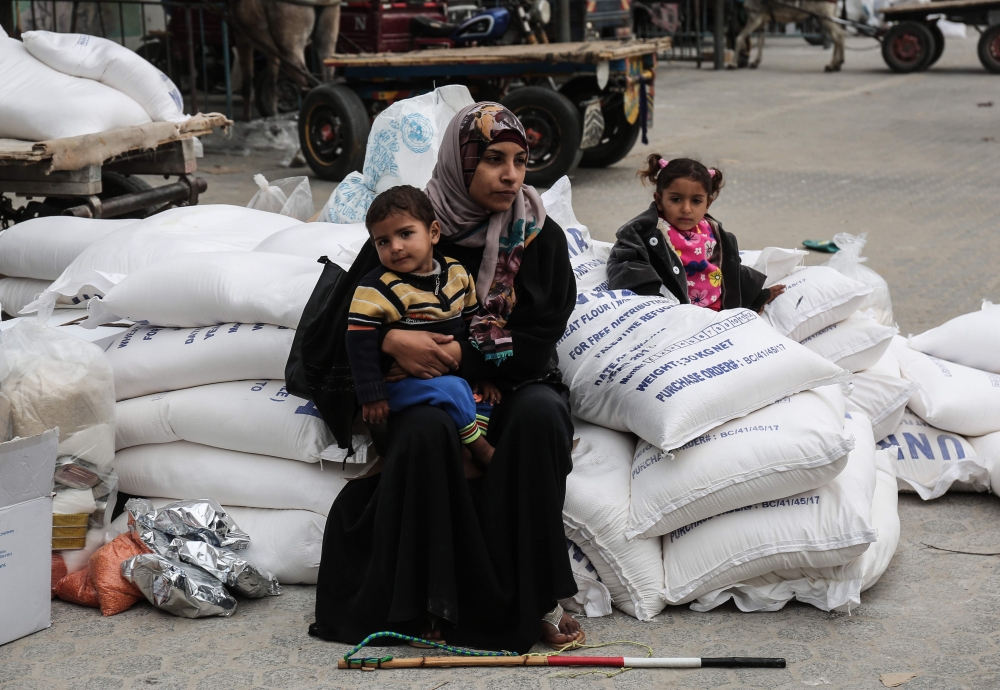 A Palestinian woman sits with a child after receiving food supplies from the United Nations' offices at the United Nations' offices in the Khan Yunis refugee camp in the southern Gaza Strip on February 11, 2018.  AFP / Said Khatib