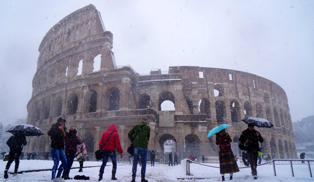 Tourists visit the ancient Colosseum during a snowfall in Rome on February 26, 2018. / AFP / Vincenzo PINTO