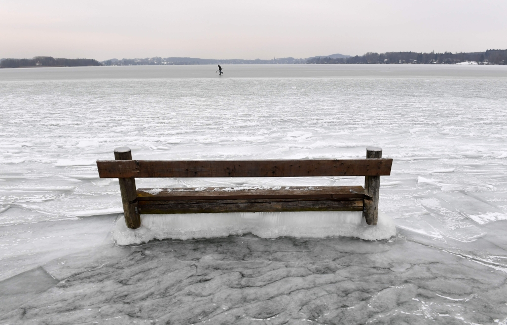 A woman ice skates behind a bench caught in the ice on the frozen Woerthsee lake on March 1, 2018 near the Bavarian village of Inning, southern Germany, as temperatures fell under minus eight degrees celsius. AFP / Christof STACHE
