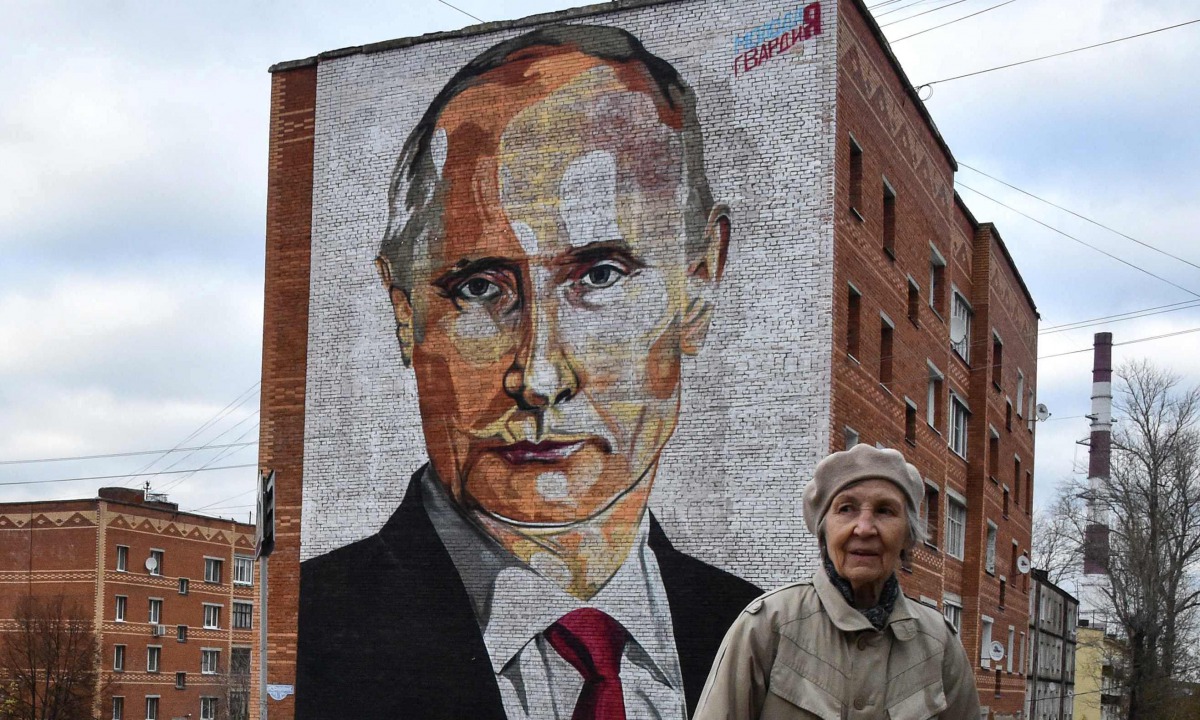 An elderly woman crosses a road in front a mural painting depicting Russian President Vladimir Putin in the town of Kashira, some 115 km southeast of Moscow on October 16, 2017. (AFP / Vasily Maximov) 