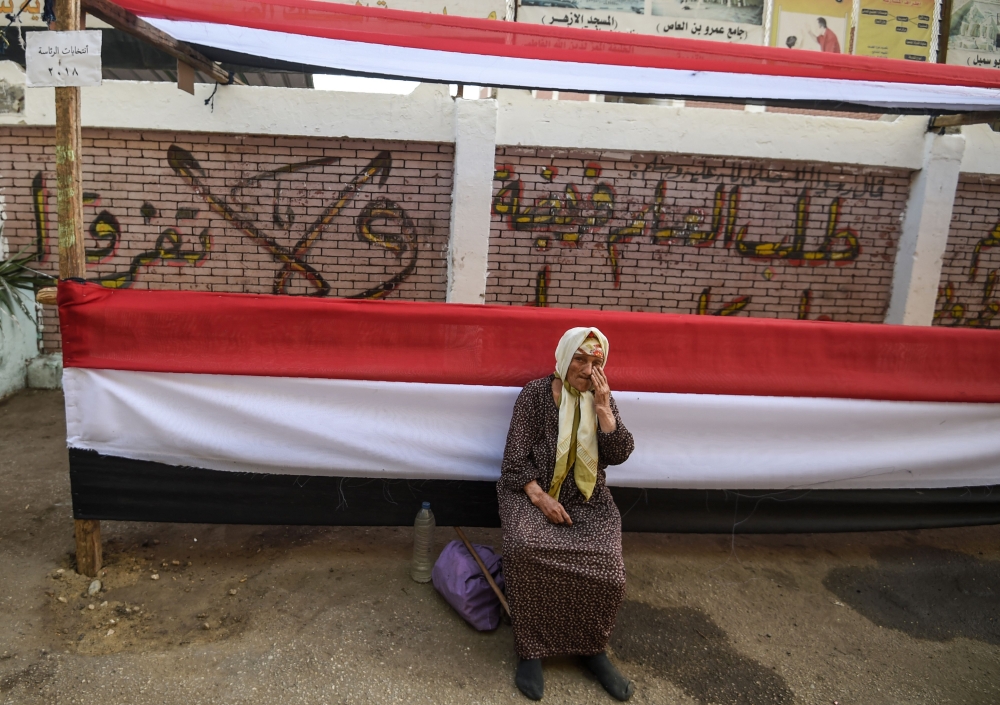 A woman sits outside a polling station decorated with long pieces of cloth depicting the colours of the Egyptian flag in the capital Cairo's central Al-Malek al-Saleh district on March 25, 2018 ahead of the vote scheduled for the following day. AFP / Moha