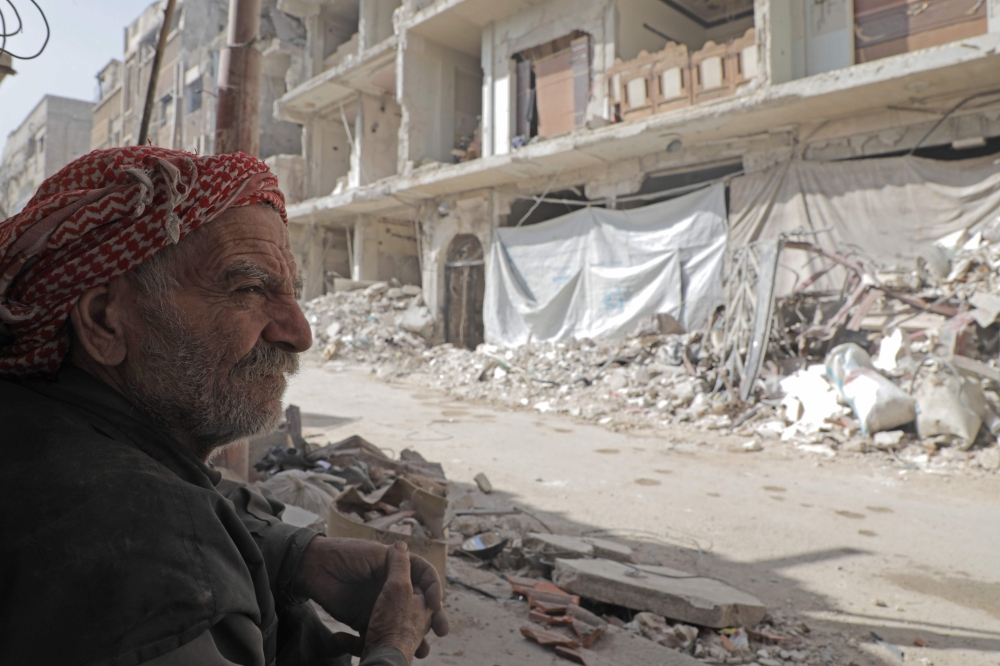 A Syrian man looks at a street and destoyed buildings following air strikes on March 25, 2018, in Douma, in Eastern Ghouta on the outskirts of the capital Damascus. AFP / HAMZA AL-AJWEH
