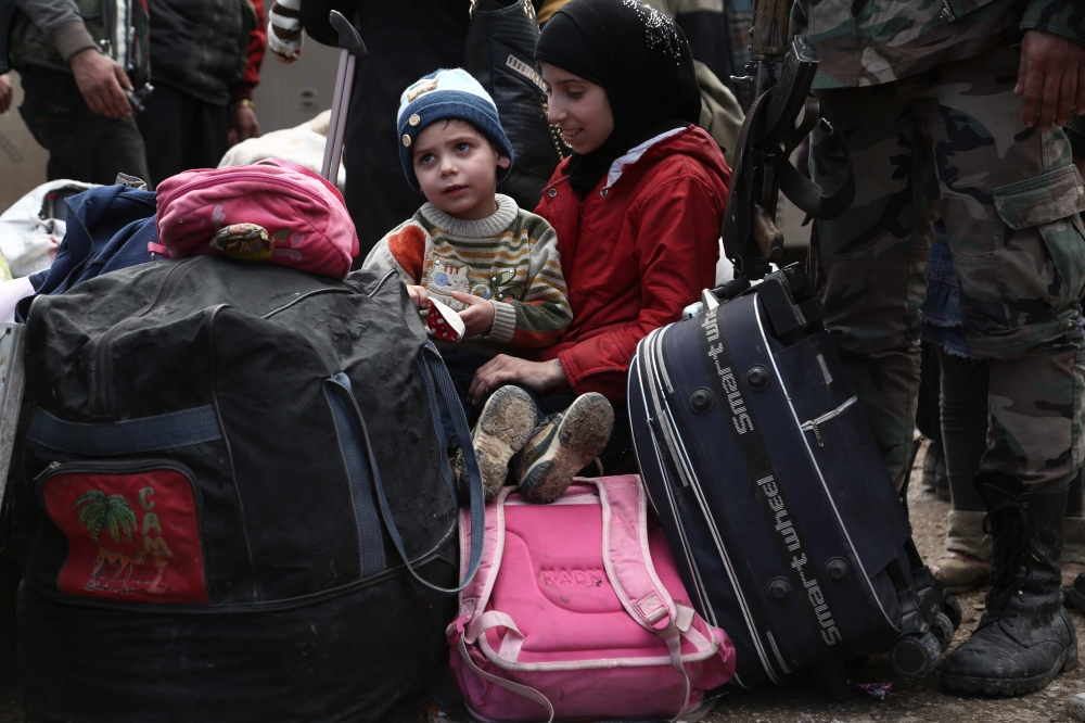 Syrian children evacuated from Eastern Ghouta sit on luggage after arriving in Qalaat al-Madiq, some 45 kilometres northwest of the central city of Hama, on March 30, 2018, following the ongoing evacuation deals made between rebel fighters and Russia, an 