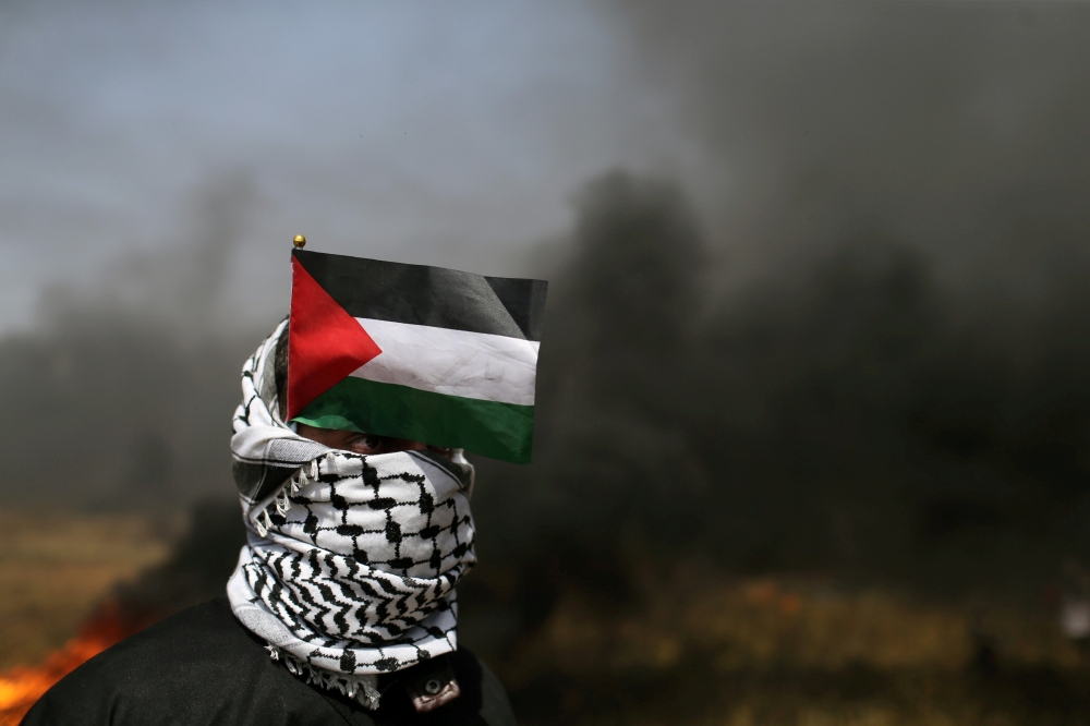 A demonstrator with a Palestinian flag looks on during clashes with Israeli troops at the Israel-Gaza border at a protest demanding the right to return to their homeland, in the southern Gaza Strip April 6, 2018. Reuters/Ibraheem Abu Mustafa 