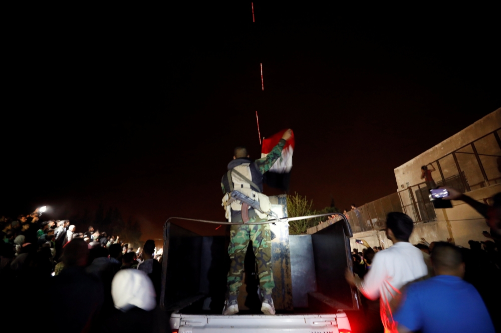A member of forces of President Bashar al Assad holds a Syrian flag as buses carrying freed hostages and rebels who were evacuated from the rebel-held city of Douma drive at Wafideen camp in Damascus, Syria April 8, 2018. Picture taken April 8, 2018. REUT