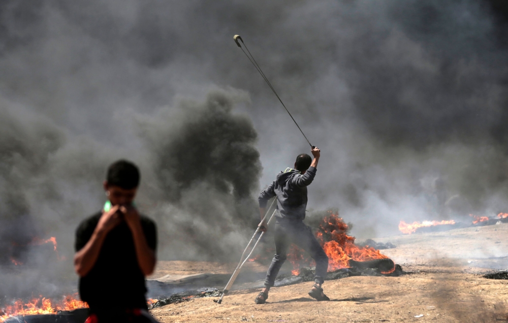 A Palestinian man uses a slingshot during clashes with Israeli forces near the border between the Gaza strip and Israel east of Gaza City on May 14, 2018, as Palestinians protest over the inauguration of the US embassy following its controversial move to 