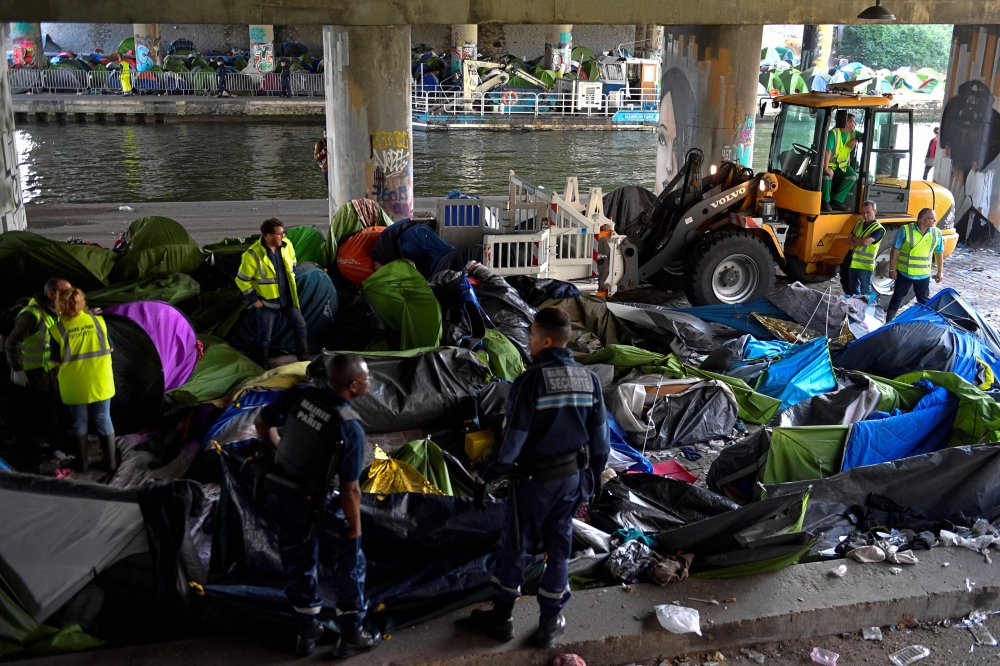 Municipal police officers of the city of Paris and workers clean up the Millenaire migrants makeshift camp along the Canal de Saint-Denis near Porte de la Villette, northern Paris, following its evacuation on May 30, 2018. / AFP / GERARD JULIEN 