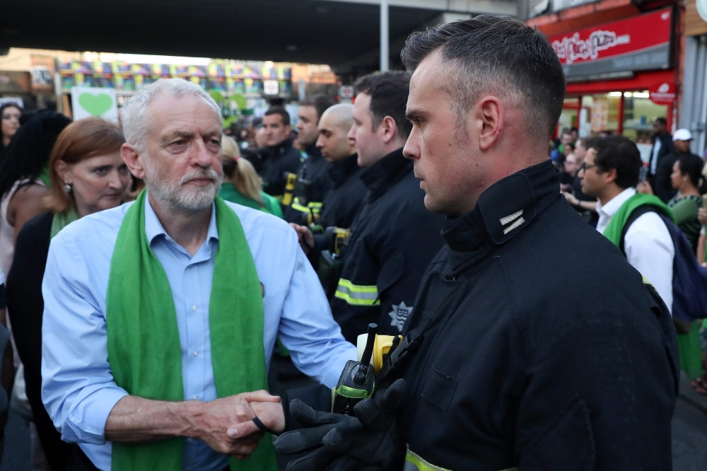 Britain's opposition Labour Party leader Jeremy Corbyn (L) shakes hands with a fire-fighter lining the street as members of the public take part in a silent march as part of commemorations on the first anniversary of the Grenfell fire in west London on Ju