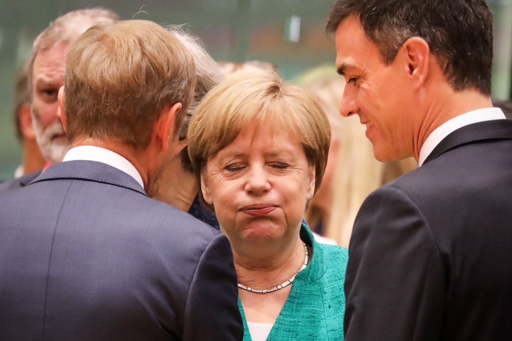 Germany's Chancellor Angela Merkel (C) reacts as she speaks with European Council President Donald Tusk (L) and Spain's Prime Minister Pedro Sanchez during an European Union leaders' summit focused on migration, Brexit and eurozone reforms on June 28, 201