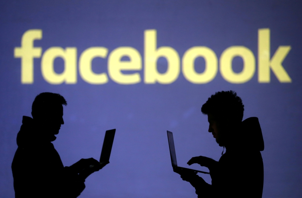 Silhouettes of laptop users are seen next to a screen projection of Facebook logo in this picture illustration (Reuters / Dado Ruvic) 