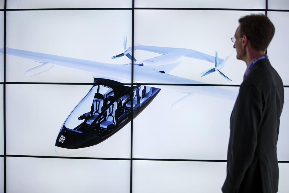 A man poses alongside screens presenting the Rolls-Royce EVTOL air taxi concept during the Farnborough Airshow, south west of London, on July 16, 2018. / AFP / Tolga AKMEN / 