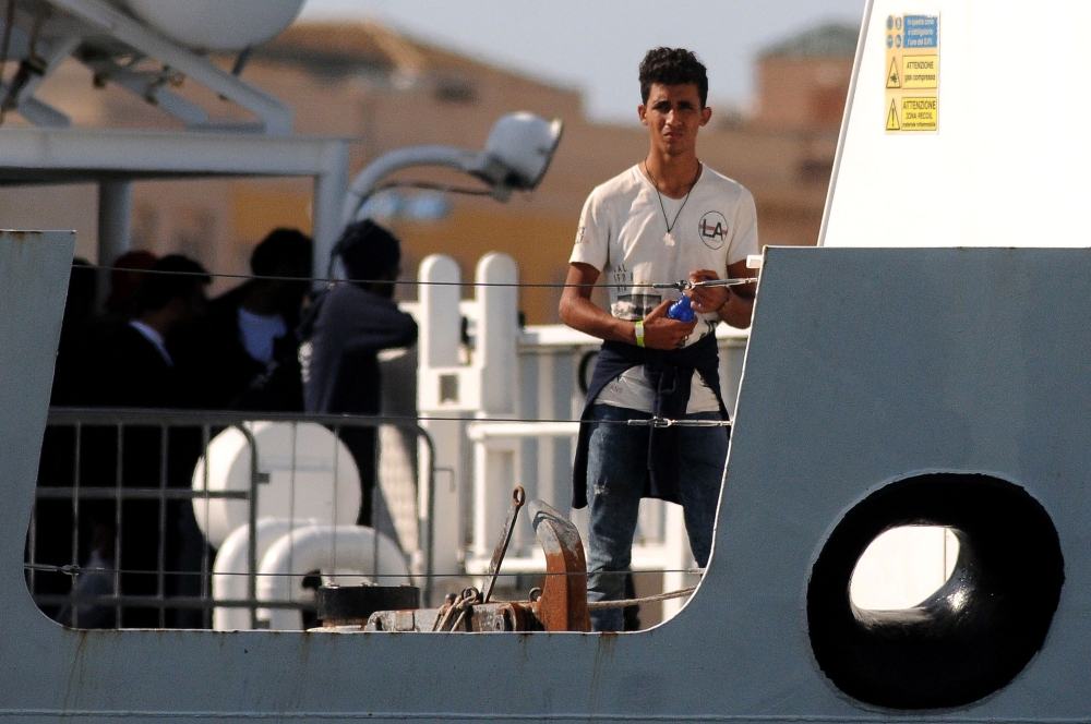 A migrant looks on from Italy's Diciotti coast guard vessel carrying 67 asylum seekers berthed at Trapani port on July 12, 2018.  AFP / Alessandro Fucarini

