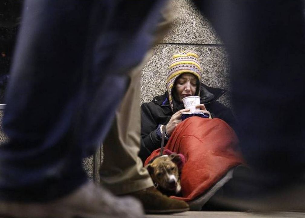 FILE PHOTO:  A homeless woman from north Wales, sits huddled under a sleeping bag next to her dog Casper in a shopping arcade near the Victoria rail station in central London December 14, 2012. Reuters/Chris Helgren