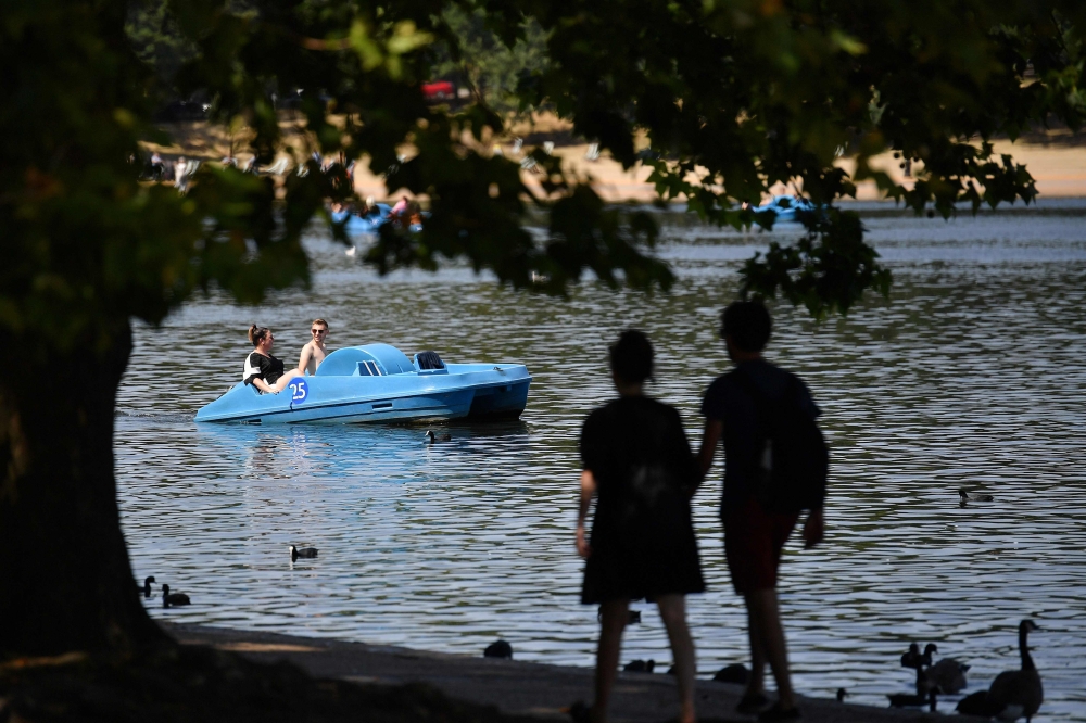 People enjoy the sunshine as thee use a pedalo on the Serpentine lake in Hyde Park in west London on August 6, 2018. AFP / Ben Stansall 