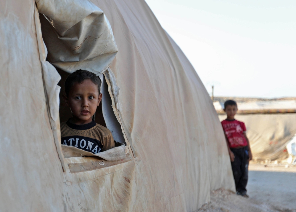A young boy peeks out of a tent in a camp for the displaced from Idlib's southern province and Hama's northern provice, in Kafr Dariyan situated at a short distance from Syria's border with Turkey, on August 26, 2018. / AFP / OMAR HAJ KADOUR
