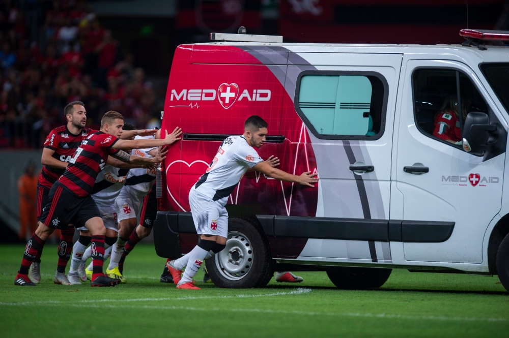 Flamengo football players Everton Ribeiro (L), Piris da Motta (C) and Brazil's Vasco da Gama player Andrey (R) and other teammates from both squads push the ambulance carrying Vasco da Gama's injured player Bruno Silva after it's engine failed to start on