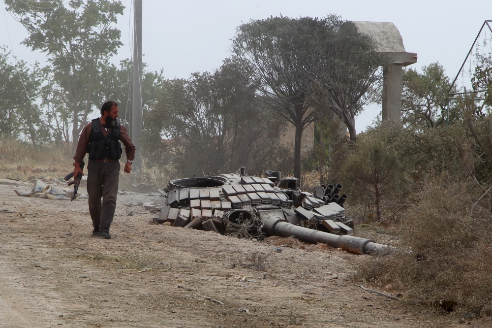 FILE PHOTO: A rebel fighter carries his weapon as he walks past the turret of a damaged tank at the Mastouma military base, after they seized it, in Idlib May 20, 2015. REUTERS/Ammar Abdullah