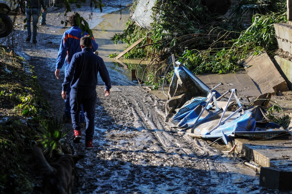 People pass on November 4, 2018 by damages on a flooded road near a house where nine people of the same family died after a small river burst its banks in Casteldaccia near Palermo on the southern Italian island of Sicily.  AFP / Alessandro FUCARINI