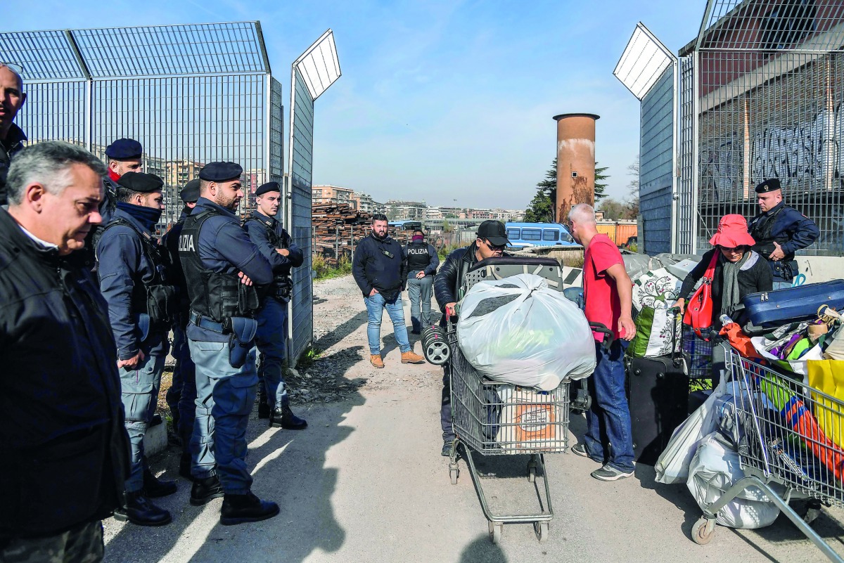 Italian Carabinieri policemen (L ad R) supervise Italian homeless citizens (C) carrying their belongings in shopping carts during the eviction of a makeshift migrants' camp known as 