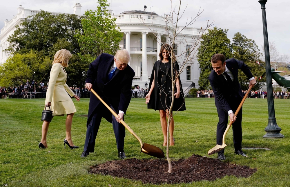 FILE PHOTO: Donald Trump and Emmanuel Macron shovel dirt onto a freshly planted oak tree as first lady Melania Trump and Brigitte Macron watch on the South Lawn of the White House, April 23, 2018. Reuters/Joshua Roberts