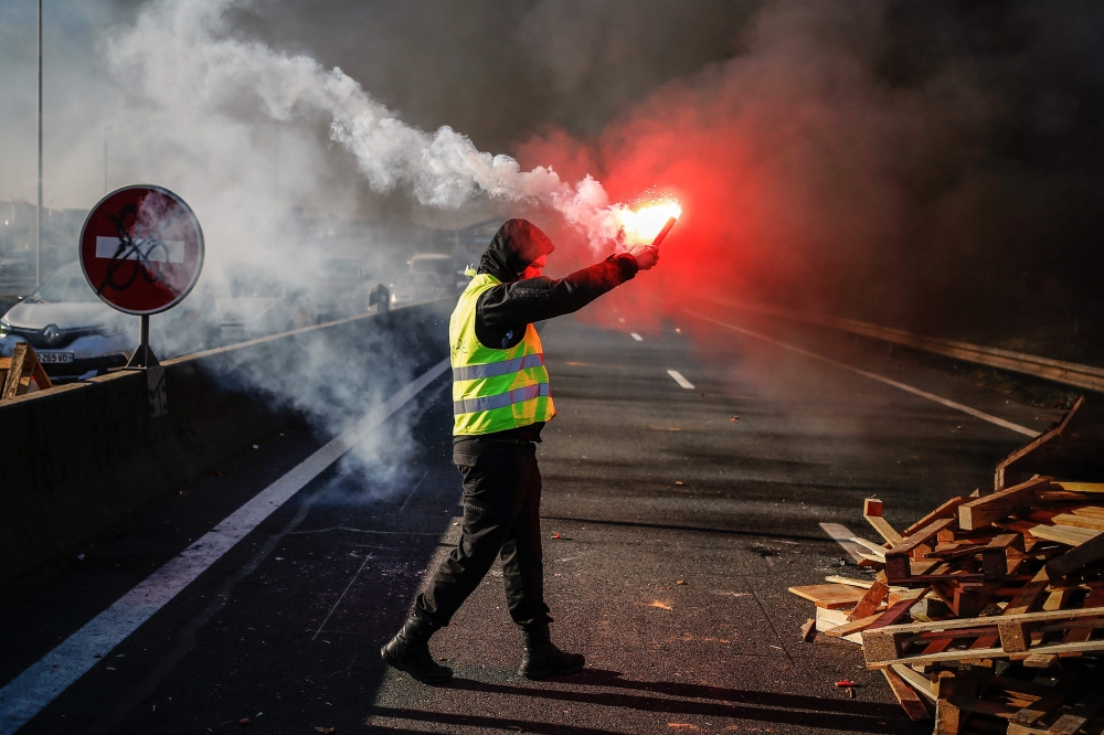 A man burn a flare as people block Caen's circular road on November 18, 2018 in Caen, Normandy, on a second day of action, a day after a nationwide popular initiated day of protest called 