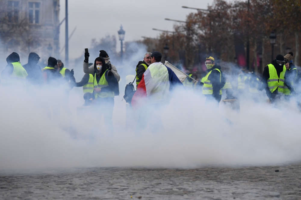 Demonstrators stand in the smoke of police grenades during a protest of Yellow Vests (Gilets jaunes) against rising oil prices and living costs on the Champs Elysees in Paris, on December 1, 2018. AFP / Alain Jocard 