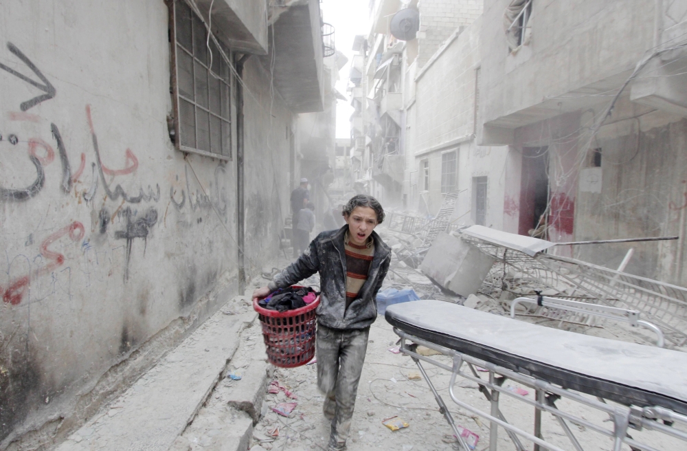 FILE PHOTO: A boy carries his belongings at a site hit by what activists said was a barrel bomb dropped by forces loyal to Syria's President Bashar al-Assad in Aleppo's al-Fardous district, Syria April 2, 2015. REUTERS/Rami Zayat