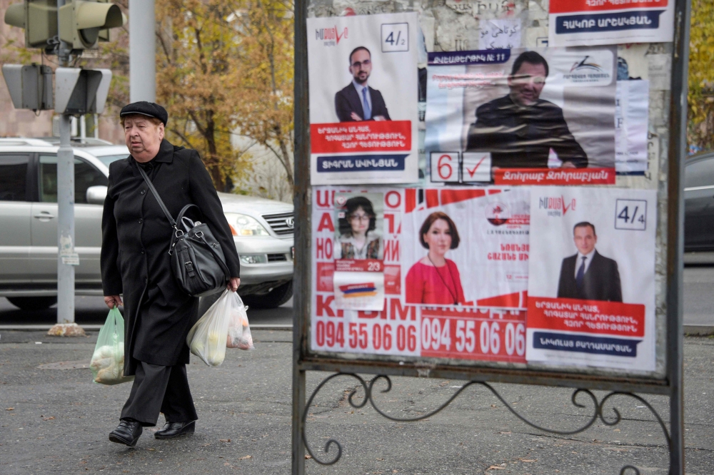 People walk past election posters in Yerevan on December 6, 2018, days before December 9 early parliamentary elections. / AFP / KAREN MINASYAN 