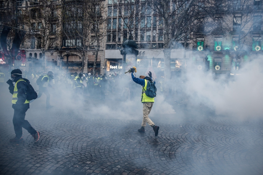 A protester wearing a yellow vest (gilet jaune) holds a bunch of flowers as he runs through smoke of tear gas during a demonstration against rising costs of living they blame on high taxes on the Champs-Elysees avenue in Paris, on December 15, 2018. AFP /