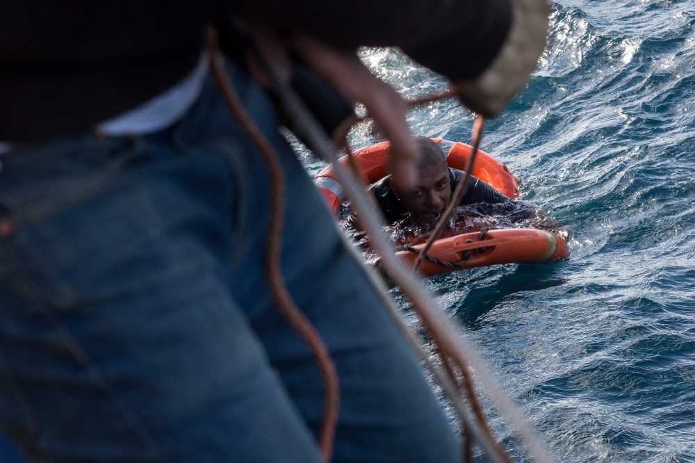 A crew member from the Dutch-flagged Sea-Watch 3 rescue vessel throws buoys and a rope to rescue a migrant back on board, after he dived on January 4, 2019 from the vessel in the cold Mediterranean off Malta's coast, in a attempt to reach the shore by swi