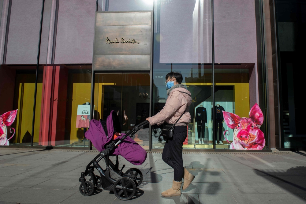 A woman walks outside of a fashion store in Beijing on January 21, 2019.  AFP / NICOLAS ASFOURI