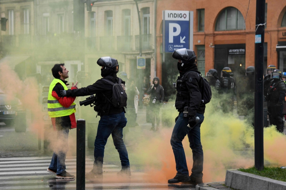 A protester speaks with French riot officers amid smoke during an anti-government demonstration called by the Yellow Vests 