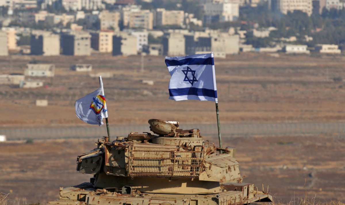 An Israeli flag flutters above the wreckage of an Israeli tank sitting on a hill in the Israeli-occupied sector of the Golan Heights on October 18, 2017. AFP/Jalaa Marey