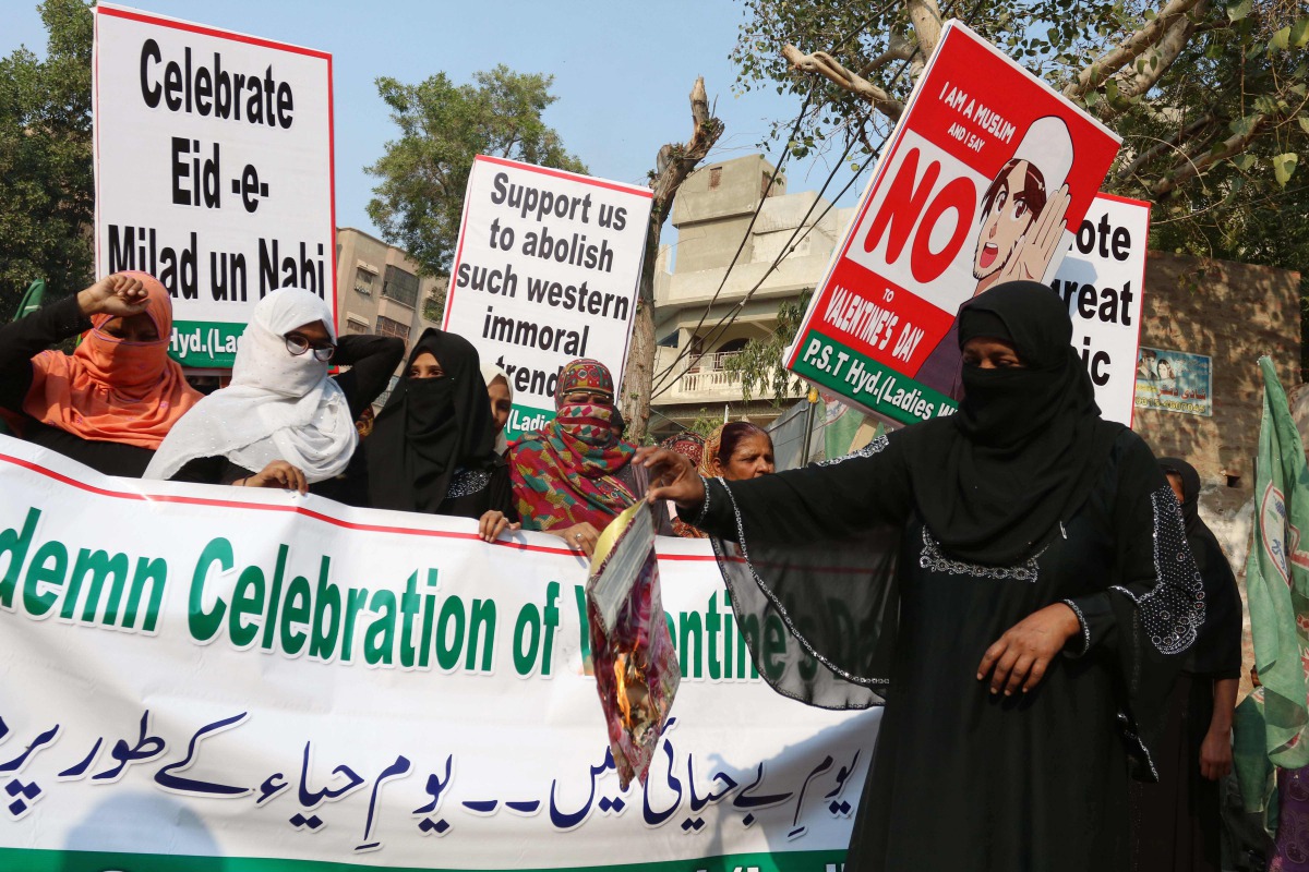 A supporter of the Pakistan Sunni Tehreek (PST) organization holds a burning Valentine's card while other carry placards and a banner during a protest against Valentine's Day celebrations, in Hyderabad on February 14, 2019.  AFP / Akram Shahid
