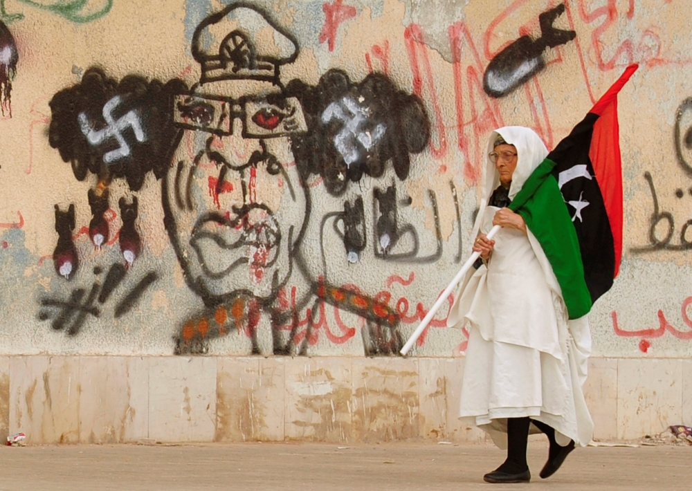A Libyan woman holding a Kingdom of Libya flag walks past a caricature of Muammar Gaddafi near the court house in Benghazi June 8, 2011. Reuters/Esam Al-Fetori