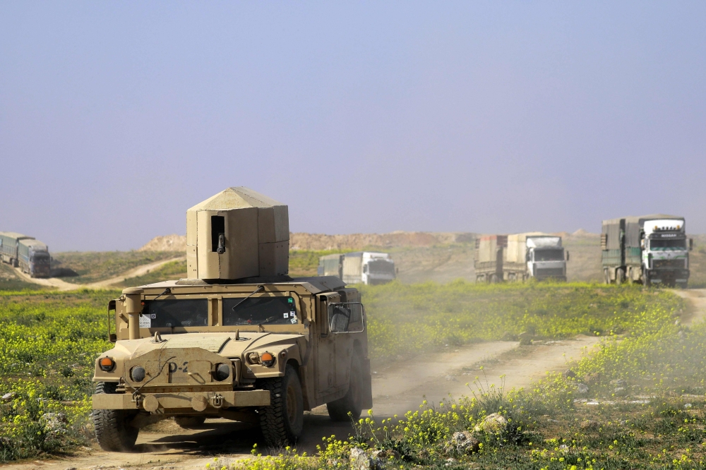Members of the Kurdish-led Syrian Democratic Forces (SDF) escort trucks carrying men, identified as Islamic State group fighters who surrendered as they are being transported out of IS's last holdout of Baghouz in Syria's northern Deir Ezzor province, on 