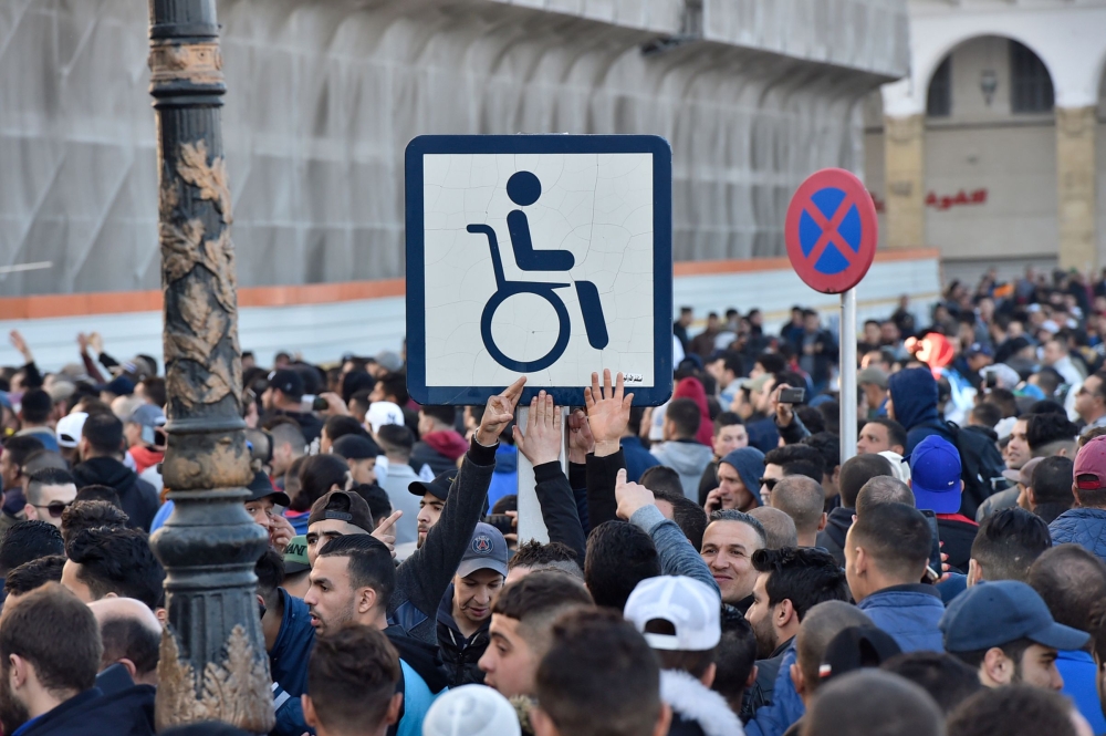 Algerian demonstrators hold a placard with the symbol of a man on a wheelchair, during a demonstration against Algeria's president's candidacy for a fifth term, on February 22, 2019 in Algiers. AFP / Ryad Kramdi 